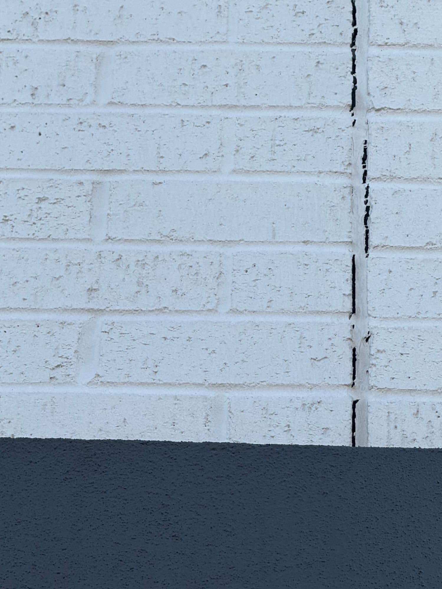 Close view of a painted brick wall with a vertical expansion joint whose old sealant has split and pulled away