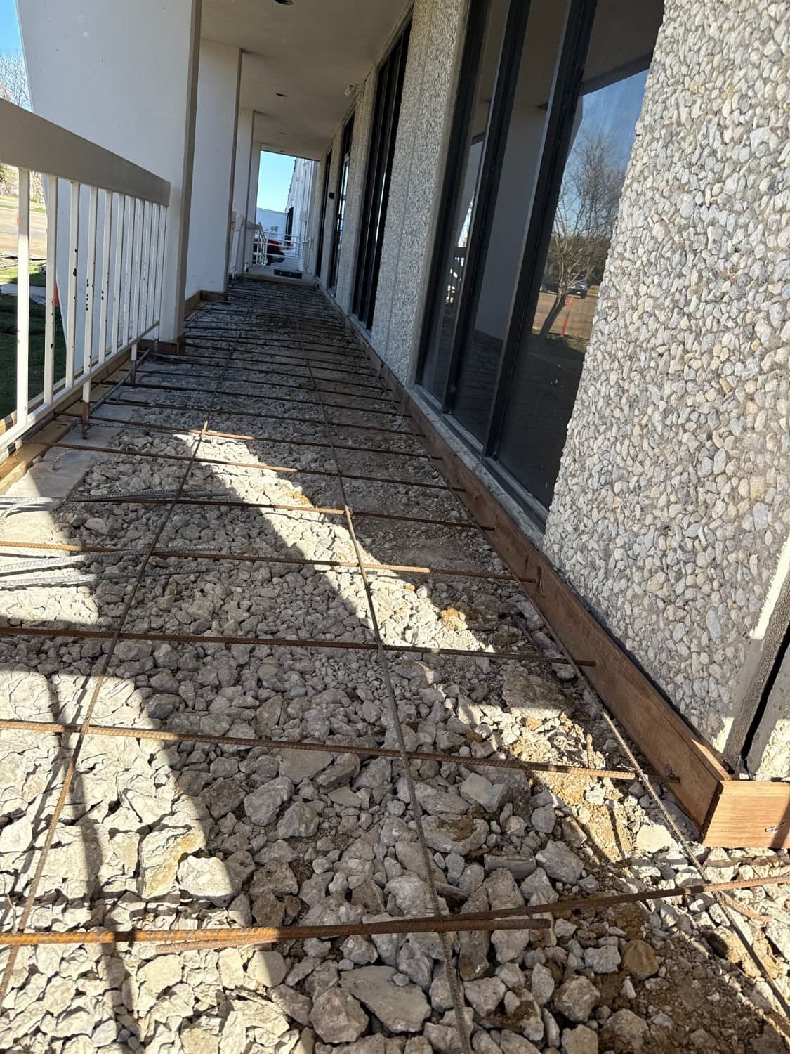 Covered walkway along an office building with forms set and steel reinforcement placed over a gravel base before concrete placement